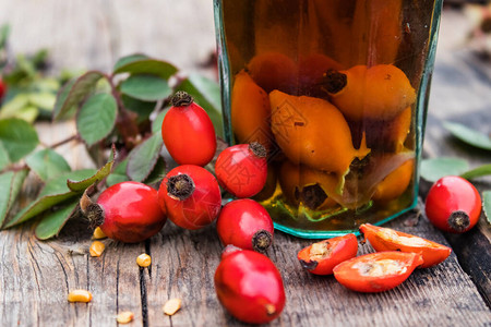 红茶玻璃瓶与酊剂或玫瑰果饮料放在靠近玫瑰果红色浆果的木桌背景