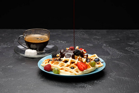 一杯加糖的黑咖啡和维也纳华夫饼草莓覆盆子醋栗和巧克力在空荡的黑色背景图片