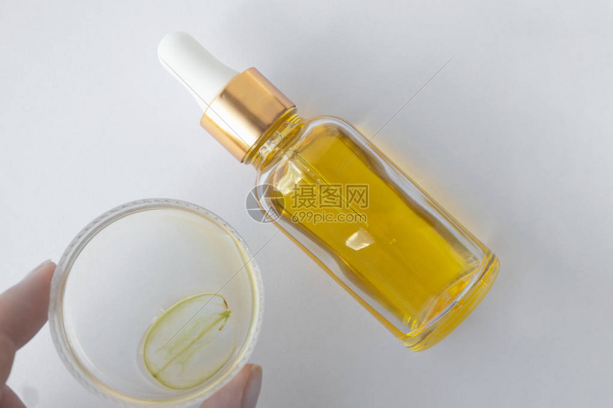 女人拿着带葡萄籽油的培养皿和白色背景上的绿葡萄片和玻璃瓶纯精华护肤油水疗护图片