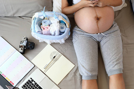 新妈为新生儿做准备的爱尿布篮子里的奶瓶笔记本电脑笔记本日程表放在床上图片