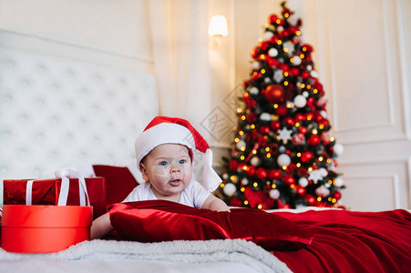 婴儿穿着圣诞老人的装扮和礼物盒躺在圣诞节客厅的床图片