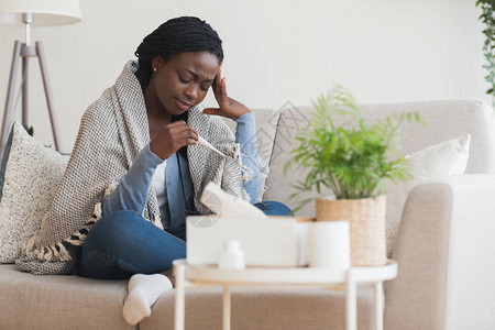 病态的非洲女人坐在沙发上与温度计图片