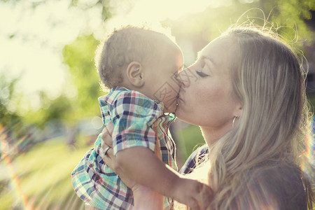 美丽快乐的母亲在夕阳的光下抱着她可爱的男婴当妈向儿子表达爱意时背景图片