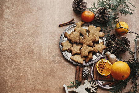 老式盘子上的圣诞姜饼干和八角生姜肉桂松果和雪松树枝在质朴的桌子上图片