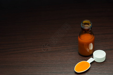 药瓶中的糖浆药物和深棕色木桌上的药勺图片