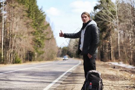 一个年轻人正在全国各地搭便车该男子正试图赶上一辆过往的汽车背着包的人搭图片