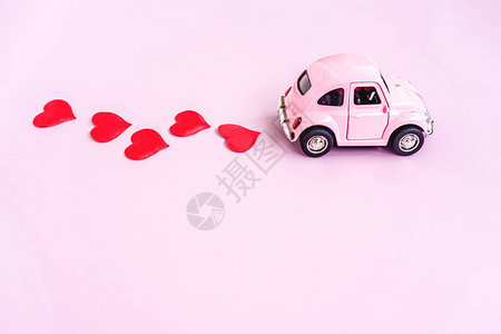 情人节用粉红背景和心胸涂面的红色小玩具车图片