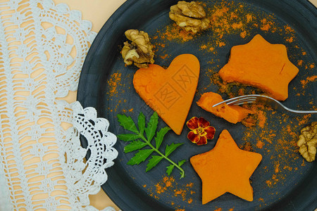 开始吃烤南瓜黑色陶瓷板与南瓜部分以心星和花的形式与手工花背景图片