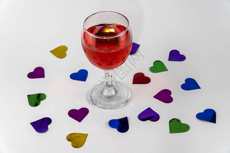 杯红酒在白色背景上散落的心形五彩纸屑情人图片