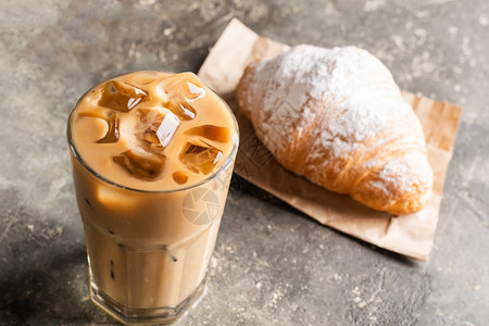 冷黑咖啡加冰块在一个高玻璃杯和新鲜的羊角面包桌子灰色背景上的清爽咖啡饮料特背景图片