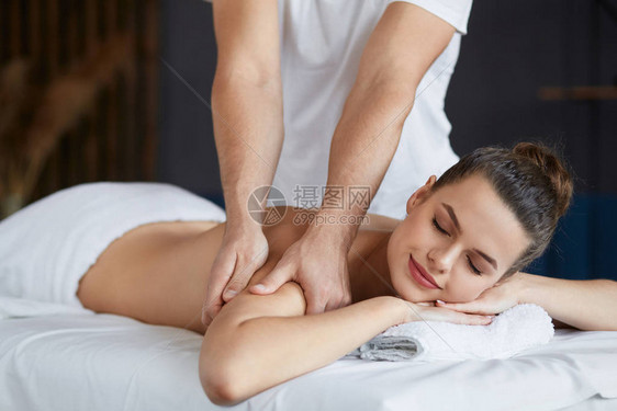 年轻漂亮的女人在水疗中心享受背部和肩部按摩专业按摩治疗师正在公寓里治疗一名女患者放松美容身体和面部治疗概图片
