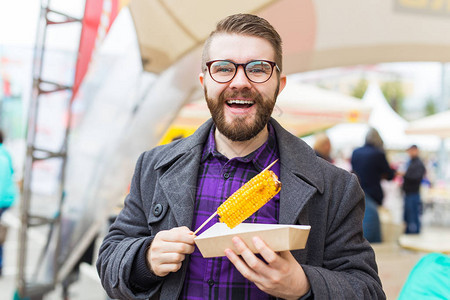 英俊的男人在快餐节吃街头食品玉米图片