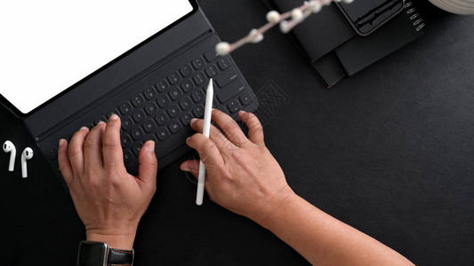 商人在数字平板电脑上打黑表背景的有tylus和其他办公用品的黑桌背景图片