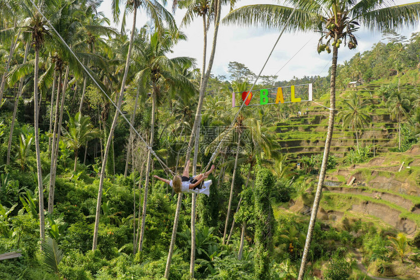 一个年轻的女孩在高的峡谷上荡秋千年轻的旅游妇女在巴厘岛热带德加拉朗丛林雨的悬崖上荡秋千秋千悬挂在两图片