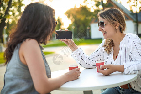微笑的成年女朋友坐在街上桌边咖啡杯和相机显示空白智能图片