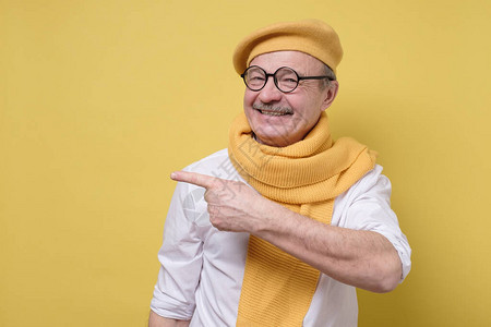 在黄色贝雷帽和围巾口中自信的老年微笑者成年男子在黄色背景上用手图片