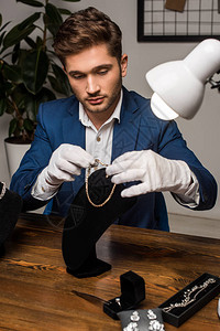 戴手套的英俊珠宝估价师在项链架附近拿着项链图片