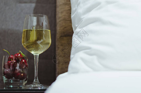 一杯白葡萄酒和樱桃水果放在桌子上除了床图片