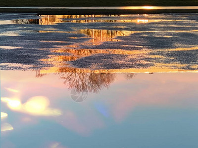 粉红金太阳光日落在城市水坑中的反射图片