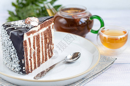 一片带有巧克力糖衣的斑马蛋糕在浅色背景上背景是一个装有花茶的杯背景