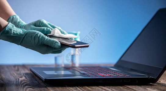 戴着无菌手套的女双手在工作场所用消毒笔记本电脑擦拭餐巾纸与作斗争背景图片