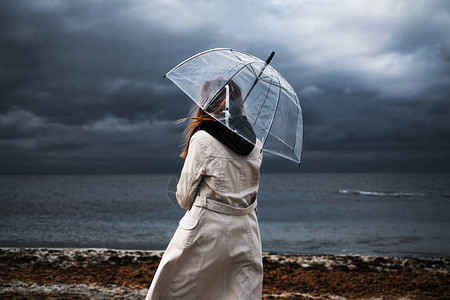 女孩在多云的天气里拿着透明的雨伞沿着海边的海滩散步雷暴和大雨下雨图片