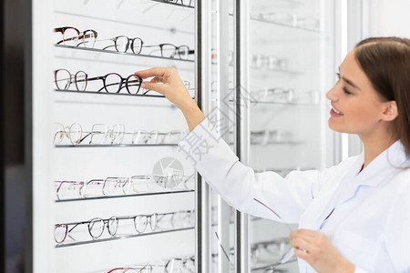 美丽的女眼科专家销售商在光学商店为客户选择眼镜框背景图片