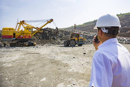 身穿白衬衫头盔的采矿工程师在花岗岩采石场监督装载自卸车图片