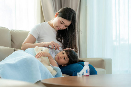 亚洲年轻母亲在家里的沙发上检查生病小女儿的体温图片
