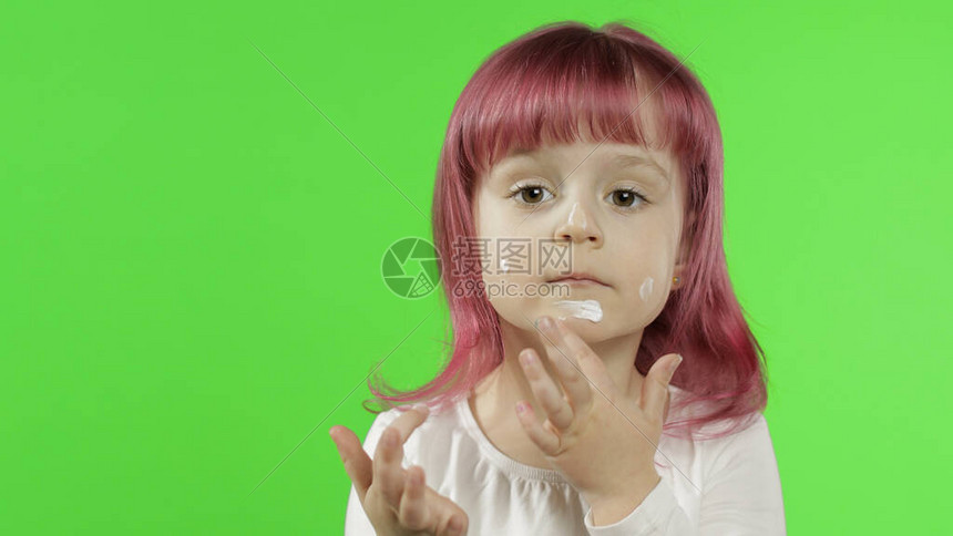 美白种儿童女孩模型与使用奶油的粉红色头发特写将奶油涂在她脸上图片