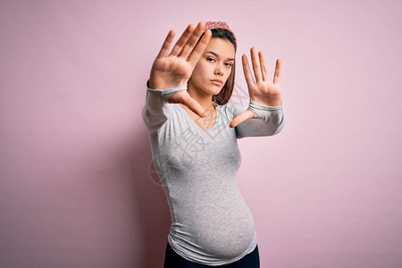 年轻漂亮的少女怀孕期待婴儿在孤立的粉红色背景下用手掌和手指做框图片
