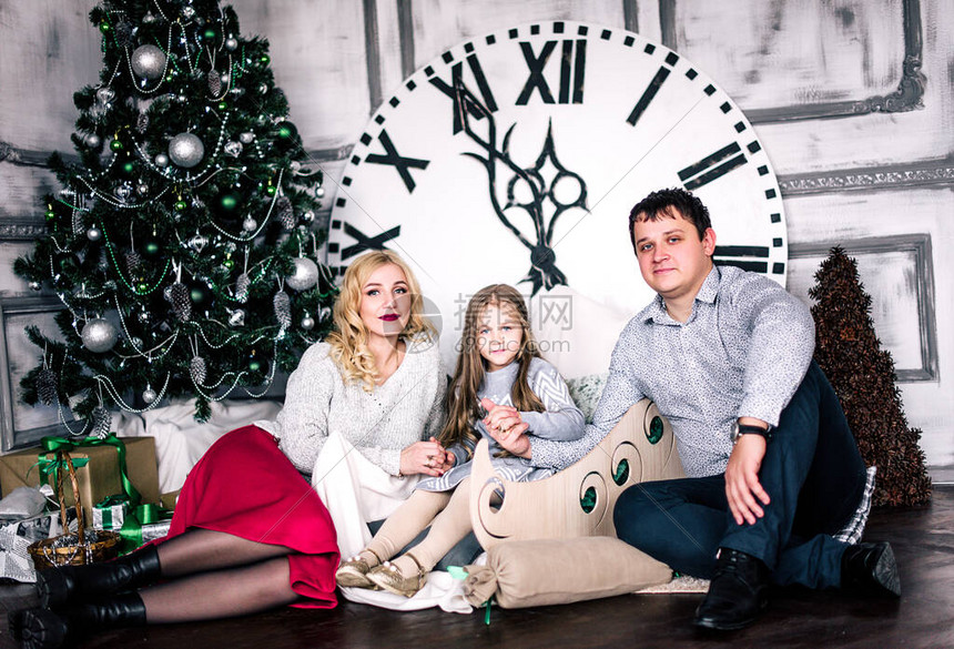 家人聚集在圣诞树附近中的时钟显示距离午夜还有五分钟平安夜新年假期和乐趣图片