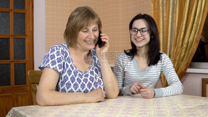 女儿教妈如何使用电话一位年轻女子向她的老母亲展示在哪里点击智能手机女人拨通了电话一家人坐在舒适的房图片