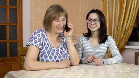 女儿教妈如何使用电话一位年轻女子向她的老母亲展示在哪里点击智能手机女人拨通了电话一家人坐在舒适的房图片
