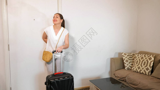 有马尾辫的漂亮女士带着大手提箱进酒店房间笑着看图片