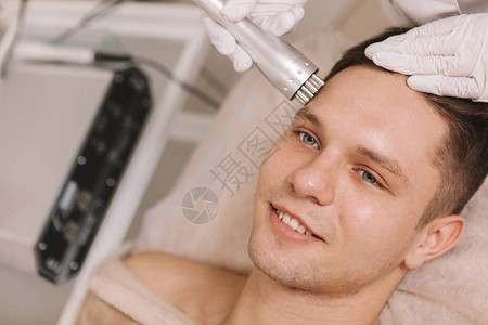 在美容院接受超声波面部皮肤护理治疗的快乐英俊的图片