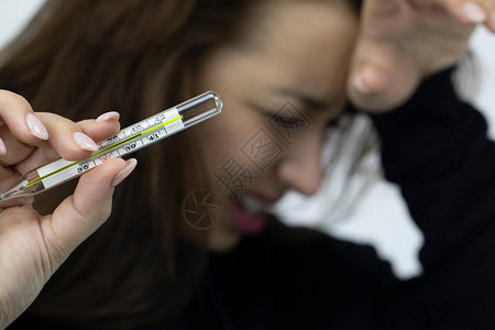 头疼的哭泣的病女孩拿着高温的水银温度计专注于玻璃医用温度计检查体温是否有症状背景图片