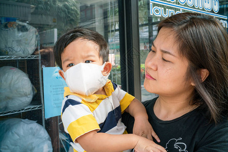 身着N95面罩的亚洲可爱男孩和母亲在户外城市建筑中保护Corona和空气污图片