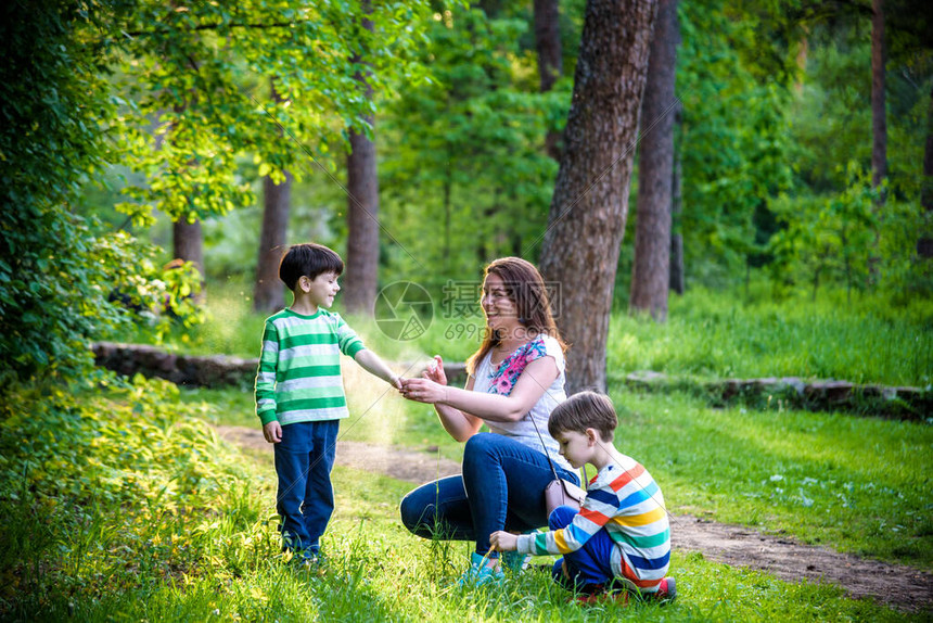 年轻女子母亲在美丽的夏日或傍晚的远足前给她的两个儿子使用驱虫剂夏季保护儿童免受昆虫叮咬与孩子图片
