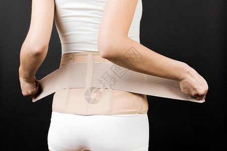 穿着支撑绷带的孕妇在黑色背景下穿上支撑绷带以减少背痛的后视图图片