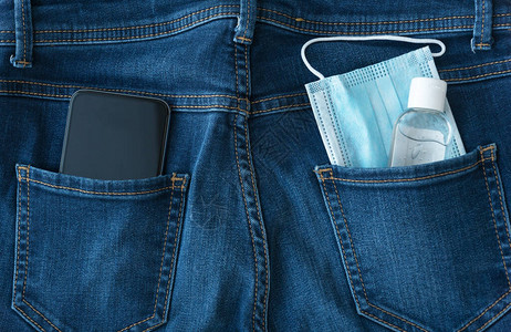 蓝色医用口罩一瓶消毒剂和黑色智能手机从蓝色牛仔裤的口袋里向外看图片