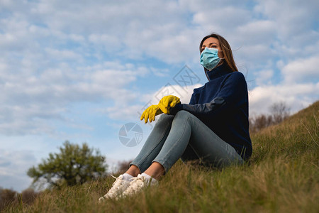 坐在绿山上戴着医用口罩和手套的美女图片