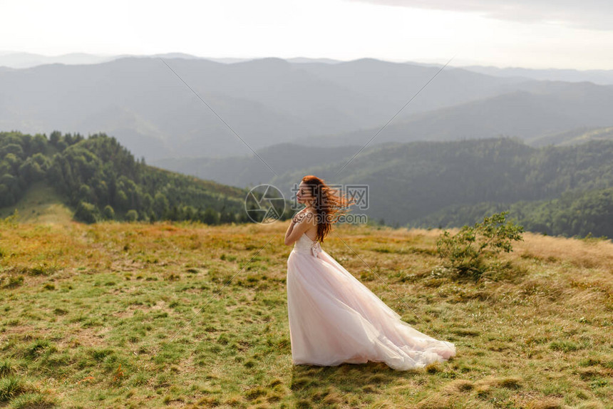 一个美丽的新娘在秋天的山脉背景上的肖像风吹动了她的头发在山顶举行的婚图片