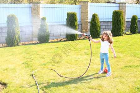 一个手里拿着软管的小女孩正在给绿色的草坪浇水一个喷壶里的孩图片