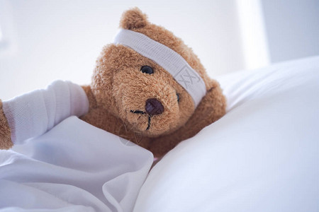 泰迪熊病倒在床上头带和布盖着图片