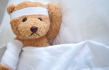 泰迪熊病倒在床上头带和布盖着图片