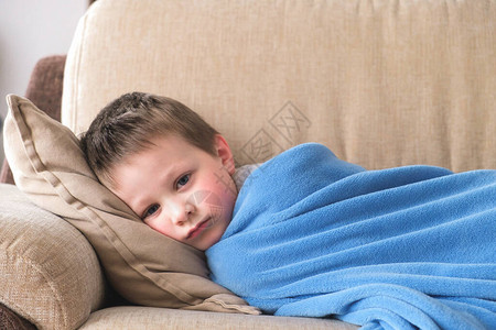 一个生病或悲伤的学龄前小男孩躺在用蓝色格子布包裹的沙发上儿童疾病抑郁疏离图片