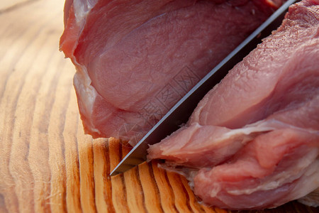 用刀在木板上切一块生猪肉图片