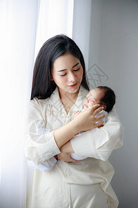 亚洲年轻的母亲在白色的卧室里抱着一个刚出生的可爱婴儿妻子抚养孩子的义务母亲背景图片