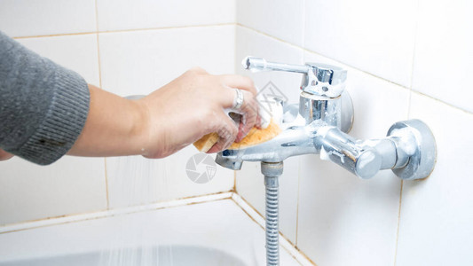 青年妇女清洁和洗浴室的水龙头或用海绵图片